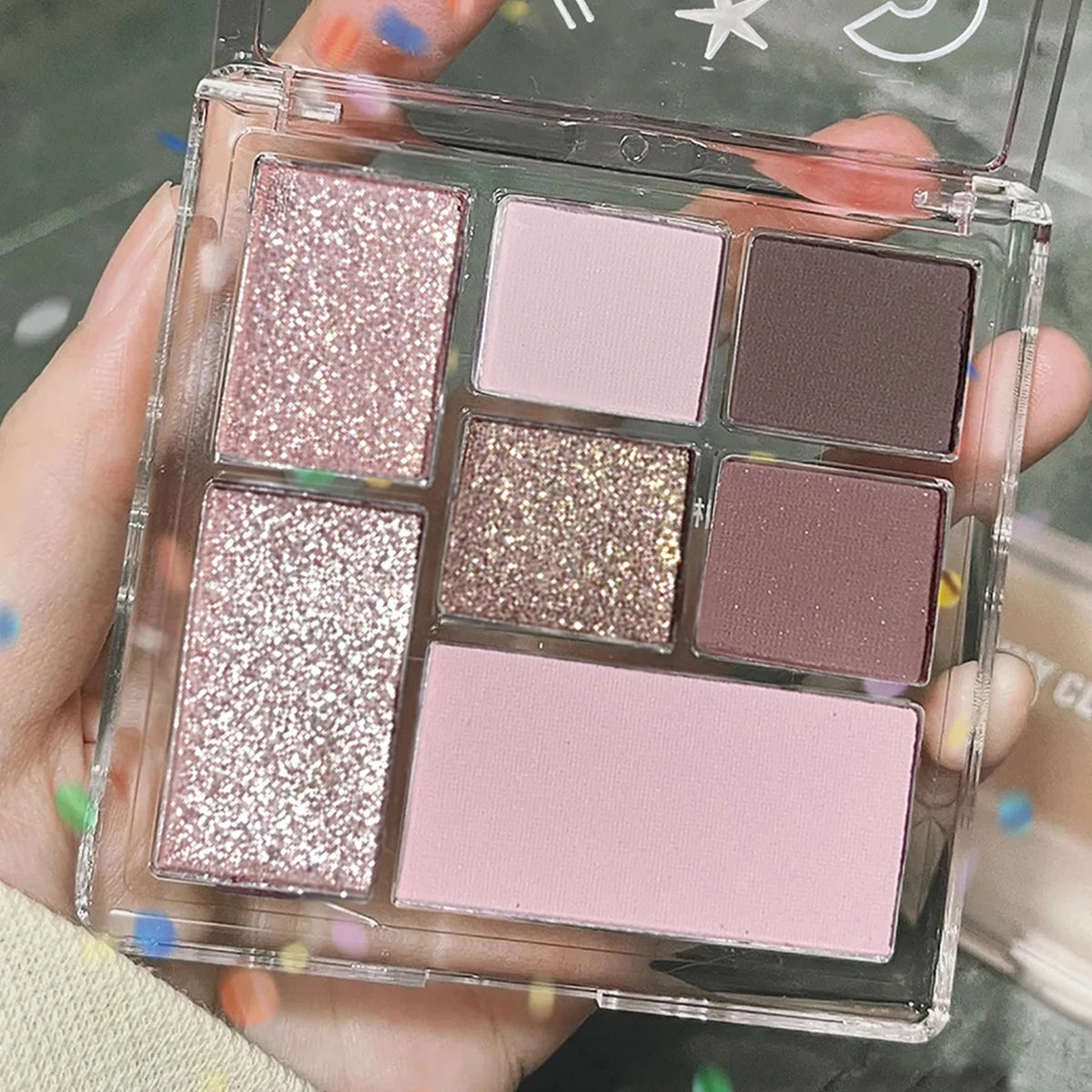 Seven-color eyeshadow palette in earth tones with shimmer, glitter, matte, and pearl finishes, waterproof, and playful
